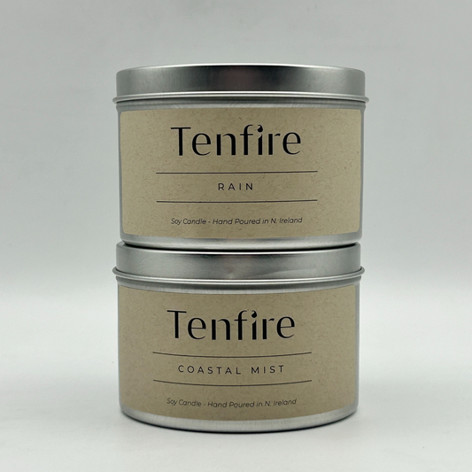 Two silver soy wax candle tins called Rain and Coastal Mist stacked on top of each other